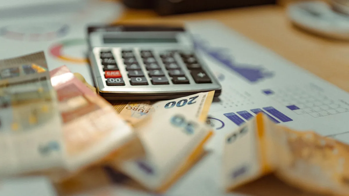 A calculator, money, and a document with a bar graph on a wooden table.