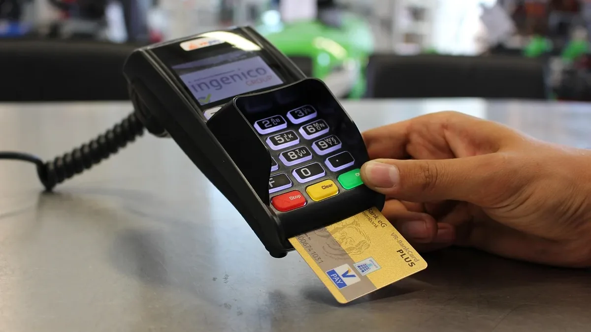 A hand holding a credit card near a point-of-sale device.